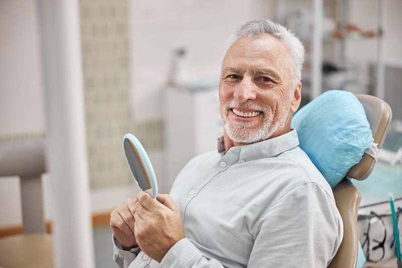 cheerful-patient-sitting-dental-chair-holding-mirror-while-smiling-camera.jpg
